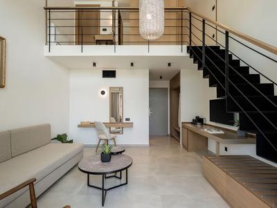 Modernes Hotelzimmer mit Sofa, Couchtisch, Treppe und minimalistischer Einrichtung in hellen Tönen.