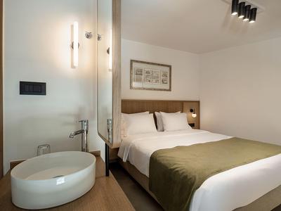 Modernes Hotelzimmer mit weißem Doppelbett, grünem Überwurf und einem runden Waschtisch.