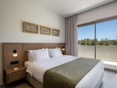 Helle und moderne Hotellandschaft mit großem Bett, drei Wandbildern und Balkon mit Naturblick.