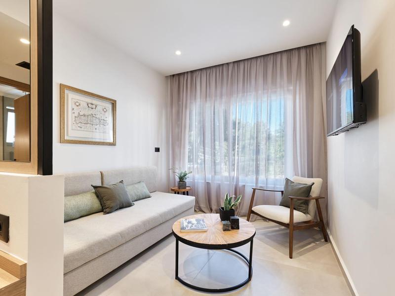 Modern eingerichtetes Wohnzimmer mit Sofa, Sessel, Couchtisch und großem Fenster mit Vorhang