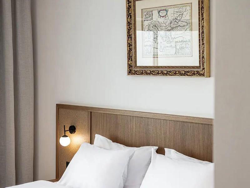 Modernes Hotelzimmer mit weißem Bett, Holzkopfteil und dekorativem Bild an der Wand.