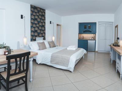 Lichte, moderne hotelkamer met tweepersoonsbed, bureau, kitchenette en schone tegelvloer.