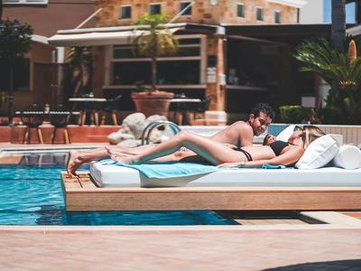 Pár odpočívá na lehátkách u hotelového bazénu za slunečného počasí.