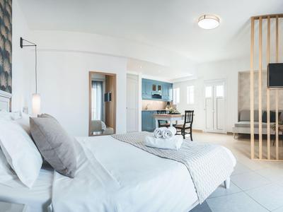 Světlý hotelový pokoj s velkou postelí, posezením a otevřenou koupelnou v moderním designu.