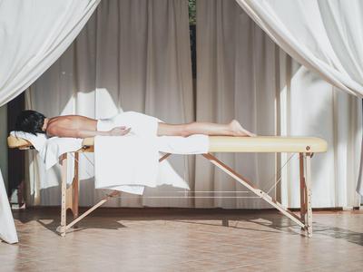 Persoon ligt op massagetafel omringd door witte gordijnen in een wellnessruimte.