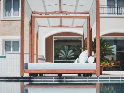 Luxusní sluneční terasa s dřevěnou postelí a bílými polštáři vedle bazénu.