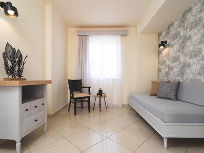 Lichte hotelkamer met grijze bank, zithoek en raam met gordijnen.