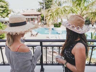 Dvě ženy s klobouky se dívají na bazén v tropickém hotelovém rezortu.