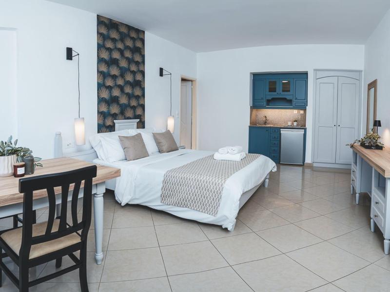 Lichte, moderne hotelkamer met tweepersoonsbed, bureau, kitchenette en schone tegelvloer.