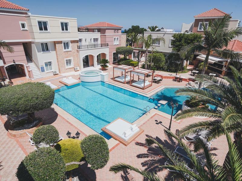 Hotelzwembad met ligstoelen, prieel en omliggende mediterrane gebouwen.