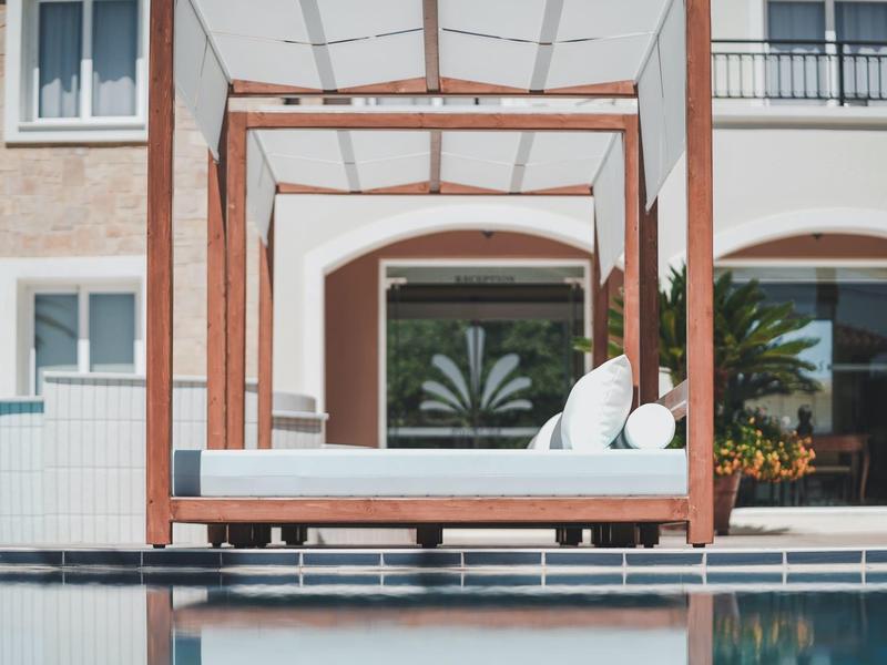 Moderne loungebed met houten constructie en witte kussens naast het hotelzwembad