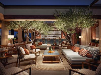 Gemütliche Lounge mit Sofas, Sesseln und Bäumen in einem offenen Raum mit Blick auf das Wasser bei Nacht.