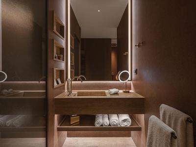 Moderní hotelový pokoj s hnědým dřevěným nábytkem, ručníky a osvětleným zrcadlem.