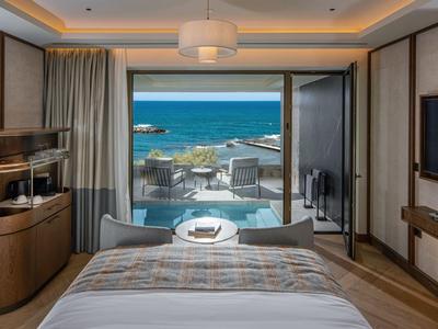 Výhled z hotelového pokoje s postelí na terasu a moře v pozadí.