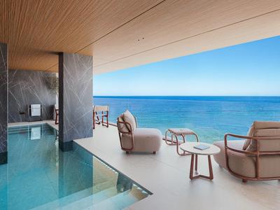 Luxusní bazénová zóna s pohodlnými křesly a výhledem na moře pod dřevěnou střechou.