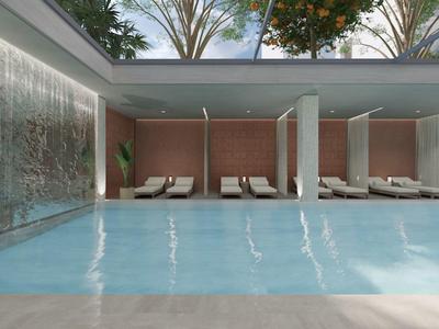 Moderní vnitřní bazén s vodopádovou stěnou a lehátky pod přirozeným světlem ze skleněné střechy