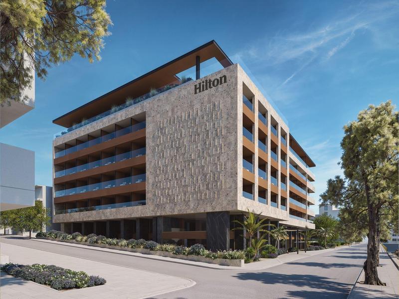 Moderní hotelová budova s balkony a logem Hilton pod modrou oblohou.