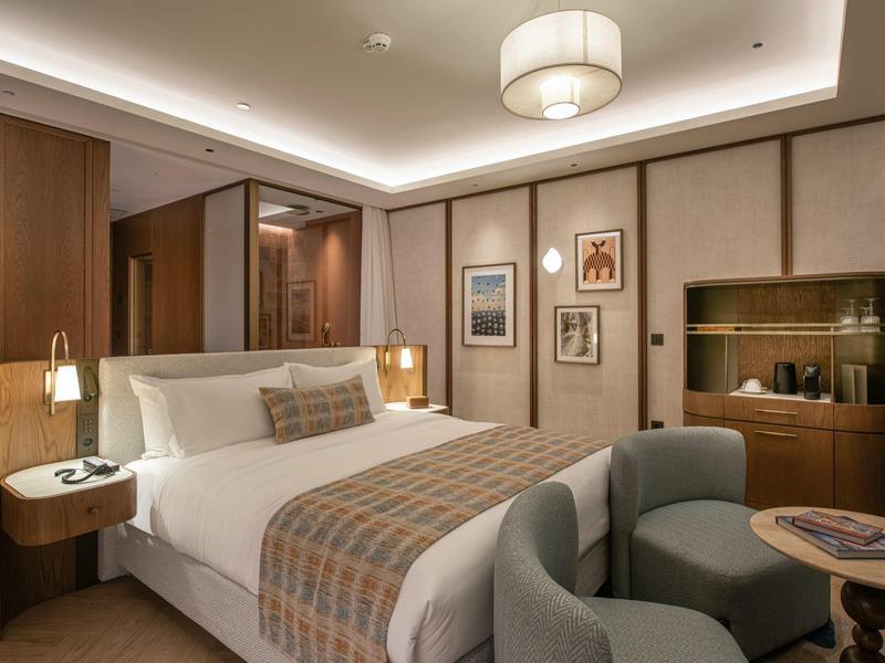 Elegantní hotelový pokoj s velkou postelí, posezením a moderním osvětlením.