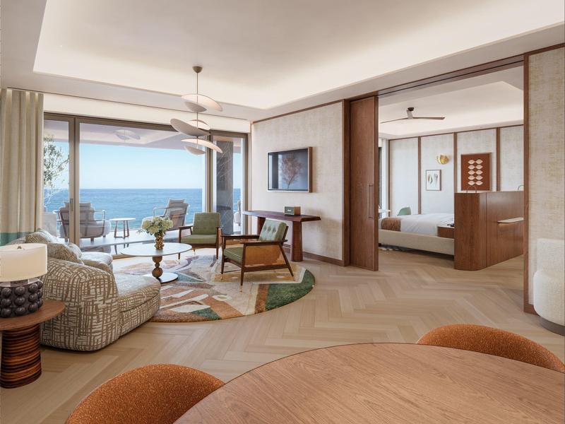 Moderní hotelový pokoj s posezením, jídelnou a výhledem na moře skrz velká okna.