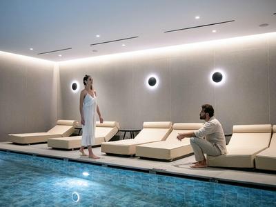 Espace bien-être moderne avec piscine et personnes en peignoirs sur des transats.
