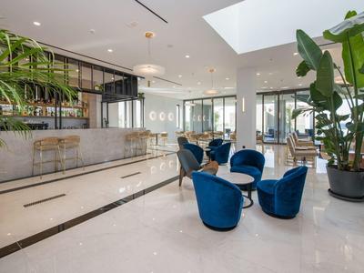 Espace lounge d'hôtel moderne avec des fauteuils bleus et un bar avec de grandes plantes.