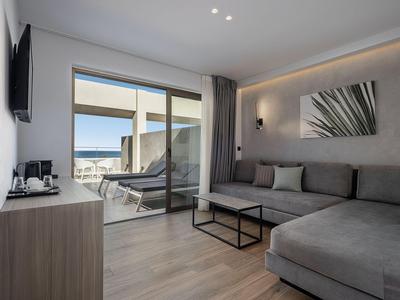 Camera d'hotel moderna con divano grigio e balcone con vista sul mare.