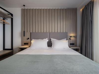 Nowoczesny pokój hotelowy z podwójnym łóżkiem, szarą wezgłowiem i panelem ściennym w tle.