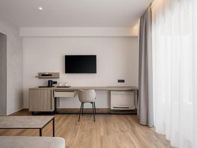 Espace de travail moderne dans une chambre d'hôtel avec bureau, chaise, TV et grands rideaux.