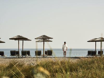 Une personne se tient sur la plage entre des parasols et des chaises longues face à la mer.
