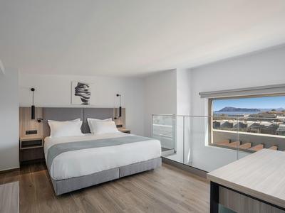 Chambre d'hôtel moderne avec lit double, tables de chevet, œuvre d'art et grande fenêtre avec vue sur la mer.