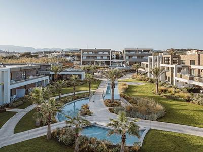 Complexe hôtelier moderne avec jardins soignés, canaux d'eau et palmiers sous un ciel clair.