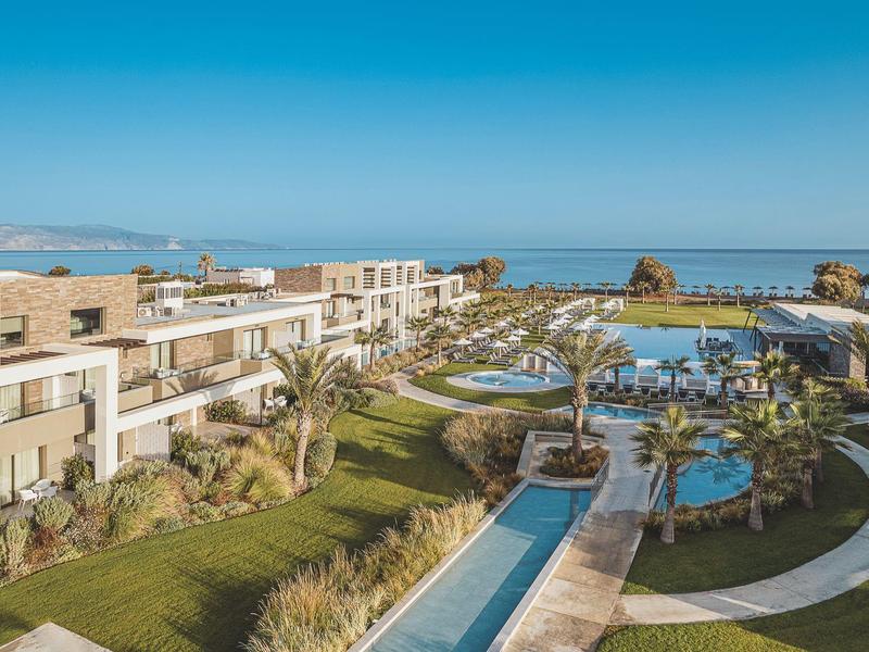 Complexe hôtelier moderne avec piscines et jardins, vue sur la mer en arrière-plan par ciel clair.