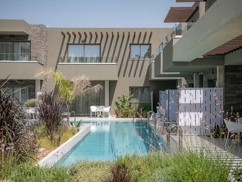 Complexe hôtelier moderne avec piscine, terrasse et plantes au premier plan sous un ciel clair.