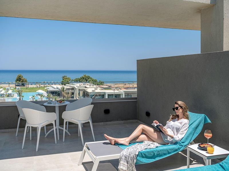 Femme se relaxant sur chaise longue sur balcon avec vue sur la mer et mobilier moderne.