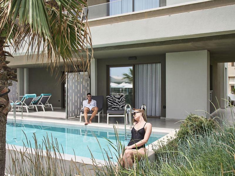 Maison de vacances moderne avec piscine, terrasse et palmiers au premier plan par temps ensoleillé.