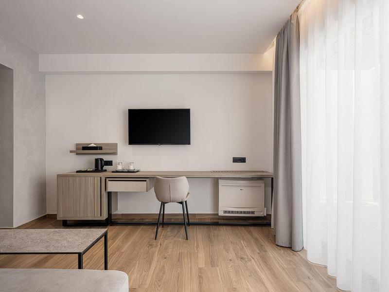 Espace de travail moderne dans une chambre d'hôtel avec bureau, chaise, TV et grands rideaux.