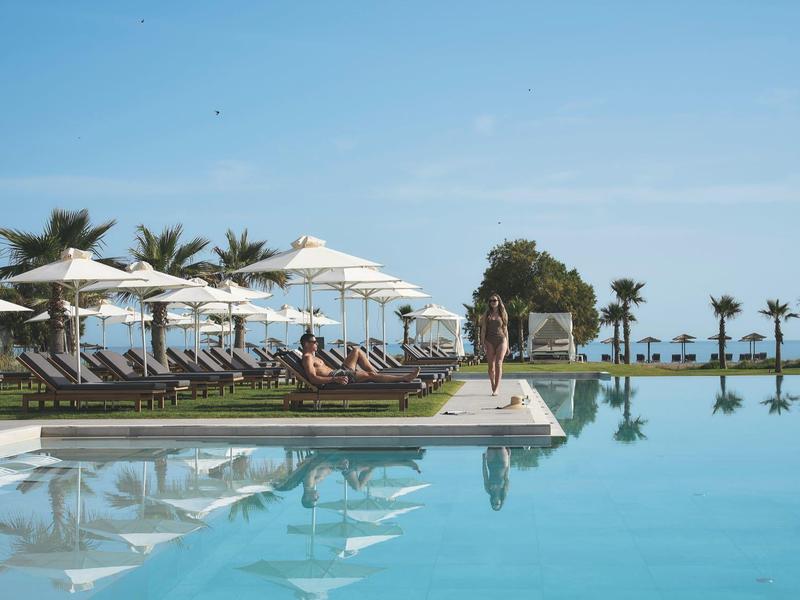 Grand bassin à débordement avec chaises longues et parasols au bord de la mer sous un ciel clair.