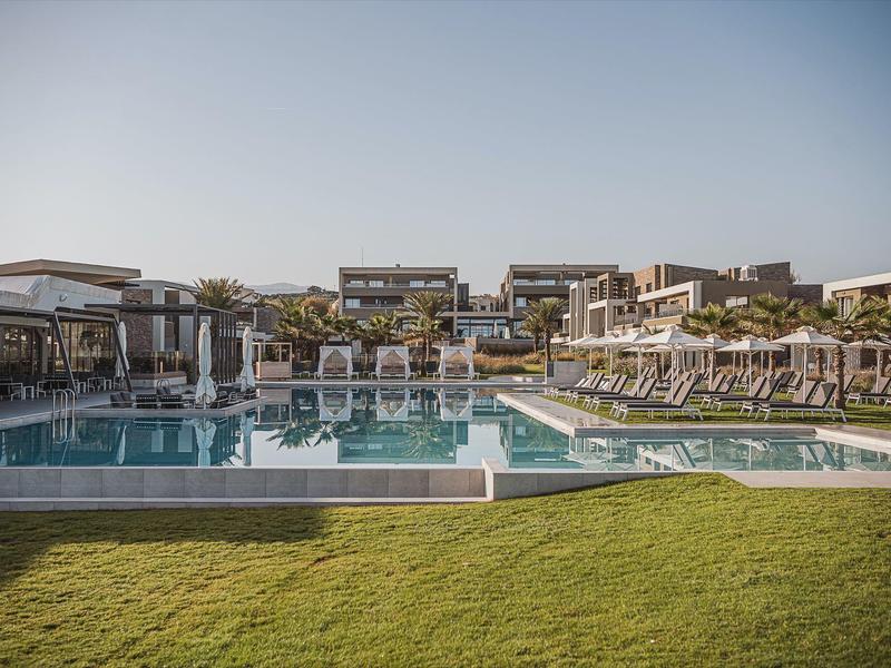 Grande piscine d'hôtel avec chaises longues et hébergements modernes sous un ciel clair.
