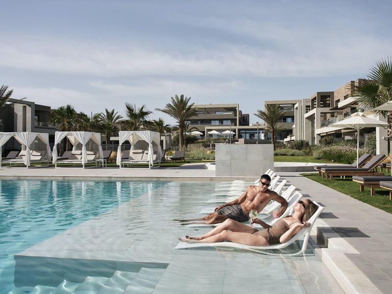 Un couple se détend sur des chaises longues au bord de la piscine d'un hôtel moderne sous un ciel nuageux.