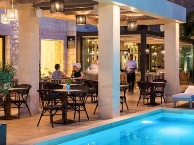 Evening outdoor area of a hotel with illuminated pool and seating under covered patio.