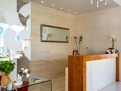Modern hotel reception area with wooden desk, mirror wall, and plants.