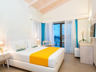 Modern hotel room with white decor, yellow bed runner, and city view.