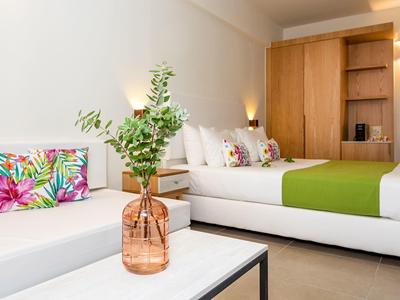 Modern hotel room with bed, sofa, colorful cushions, and vase with plant branches.