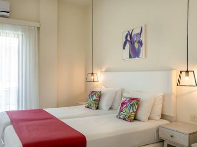 Modern hotel room with double bed, colorful pillows, and red runner next to window with curtains.