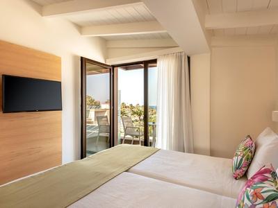 Bright hotel room with double bed, wall-mounted TV, and balcony overlooking the city.