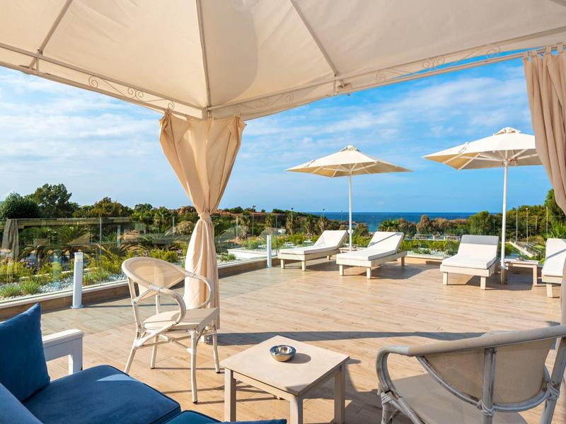 Terrace with sun umbrellas and loungers overlooking green landscape and blue sky