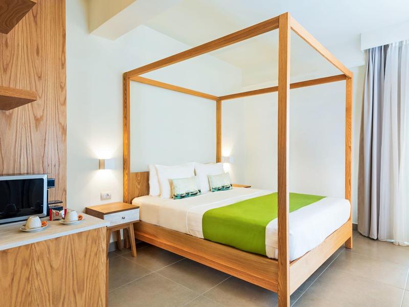 Modern hotel room with four-poster bed, desk, and large windows.