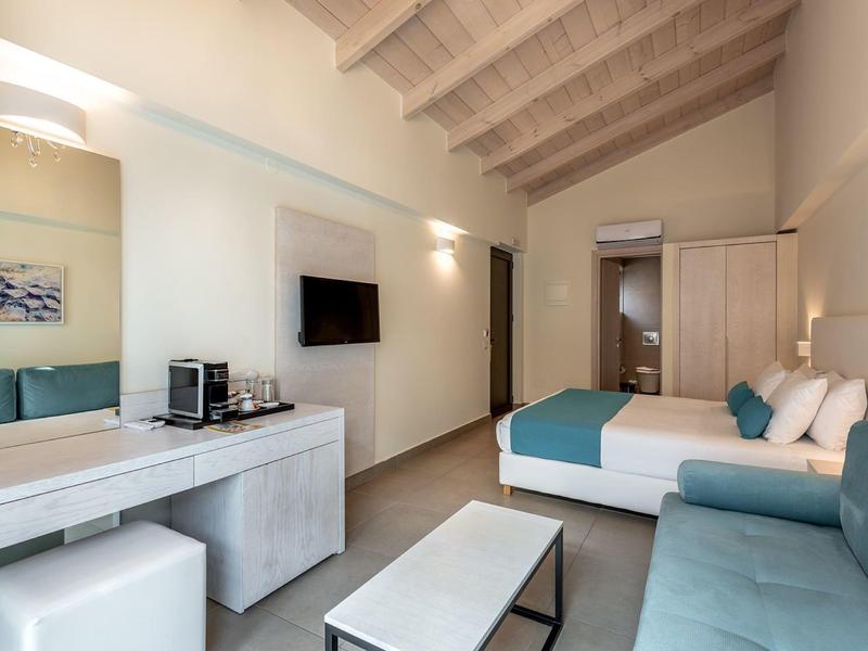 Modern hotel room with bed, sofa, desk, and television.