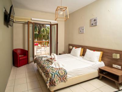 Modern hotel room with double bed, balcony, and red armchair in bright space.