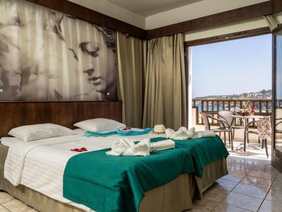 Hotelzimmer mit zwei Betten, grünem Überwurf und Balkon mit Blick auf die Stadt.